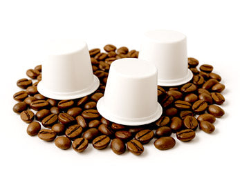 Three white coffee pods on a bed of coffee beans